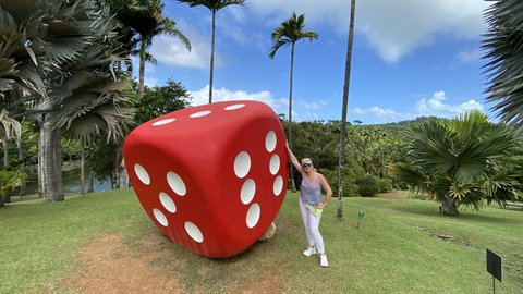 Tourist leaning on a giant red dice in a tropical garden with palms