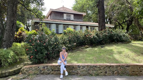 Woman sitting on a stone wall in front of a wooden Creole plantation house