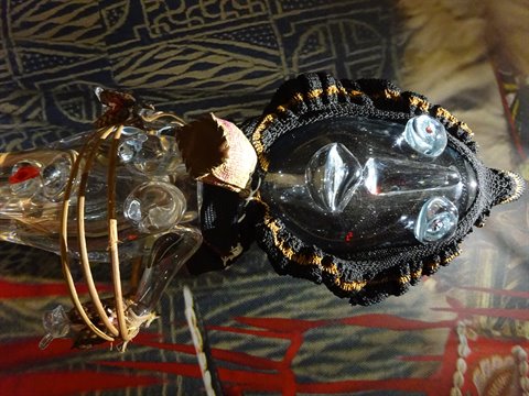 Handcrafted doll with glass mask and black embroidered fabric under warm light