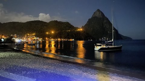 Sailboat anchored at night by the Piton, village lights reflecting on water