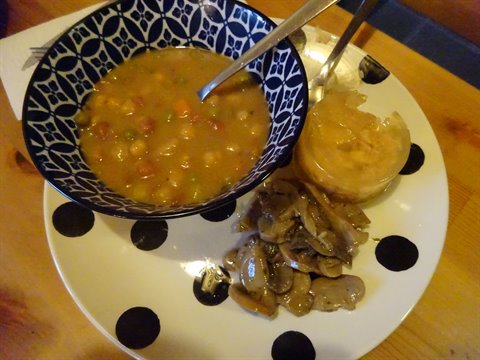 Zuppa di legumi in ciotola blu con funghi e pane, tavolo in legno