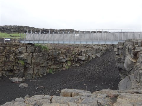 Ponte di legno tra pareti di roccia lavica nera sotto cielo grigio