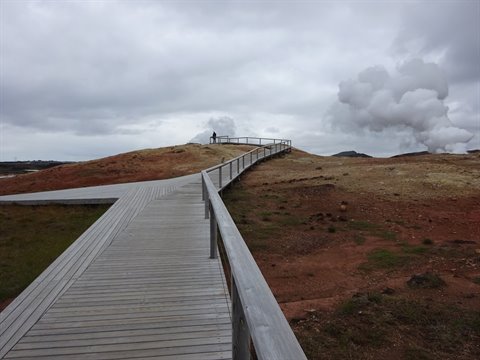 Passeggiata in legno tra i fumaroli geotermici sotto un cielo grigio