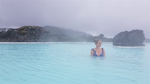 Donna in costume nell'acqua turchese della Blue Lagoon tra rocce laviche nebbiose