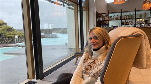 Donna in maglione islandese al bar della Blue Lagoon, laguna azzurra visibile