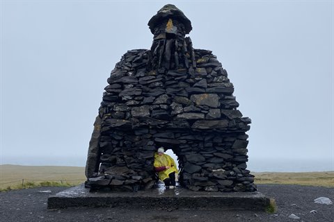 Statua di pietra di Bárður Snæfellsnes, turista con impermeabile giallo sotto l'arco