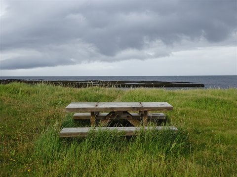 Tavolo di legmo in erba verde davanti al mare sotto nuvole grigie a Sandgerdi