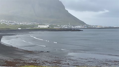 Spiaggia di sabbia scura davanti alla città sotto la montagna nuvolosa, Siglufjordur
