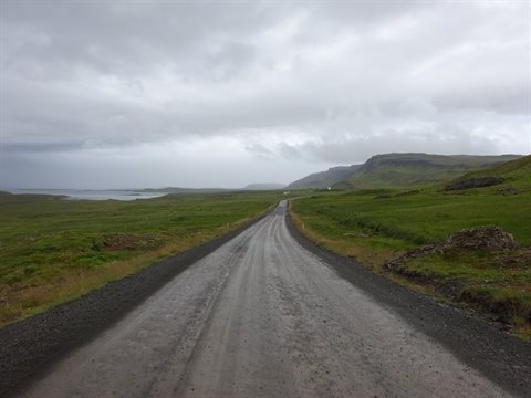 Strada sterrata bagnata verso Staðarskáli, erba verde e nuvole basse