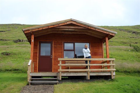 Bungalow in tronchi di legno tra le colline verdi, lei sorride sulla veranda