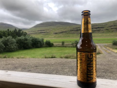 Birra Viking Gylltur su una ringhiera di legno, colline verdeggianti sotto nuvole grigie