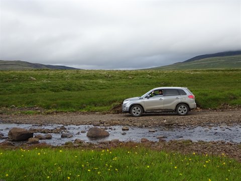 Suv 4x4 guada un torrente tra prati verdi e colline nebbiose, Islanda