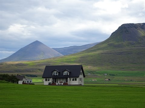 Casa isolata con tetto nero sul prato verde sotto monti nuvolosi, Akureyri