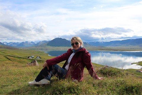 Donna seduta sull'erba davanti al lago e montagne di Myvatn