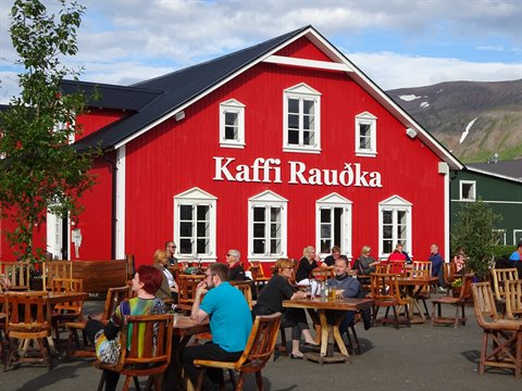 Turisti seduti ai tavolini in legno davanti alla casa rossa Kaffi Rauðka, Siglufjordur