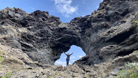 Donna con braccia alzate sotto un arco di roccia lavica a Arnastapi