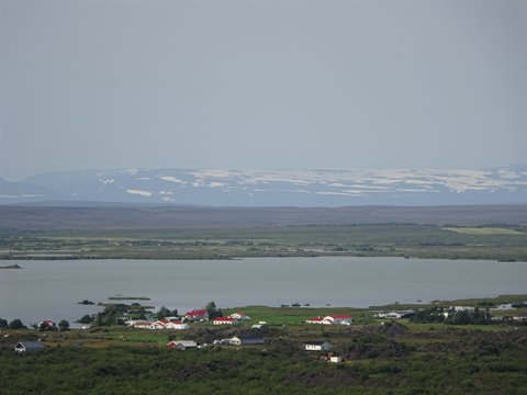 Lago Myvatn con case rosse e neve lontana sotto cielo grigio