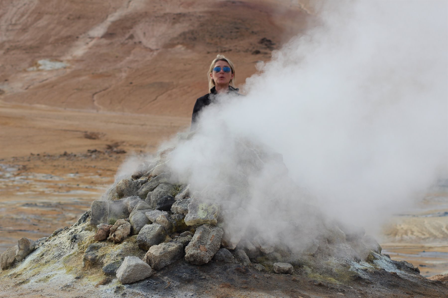 Donna con occhiali da sole tra i fumi solforosi di una fumarola a Námaskarð
