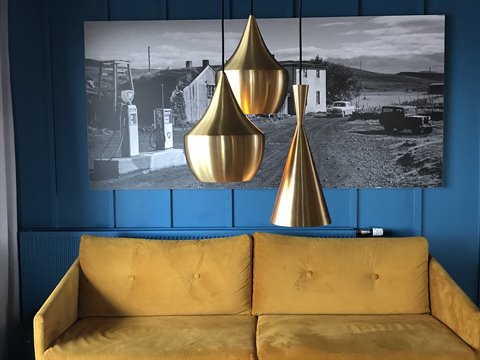 Divano giallo e lampade dorate contro parete blu con foto in bianco e nero