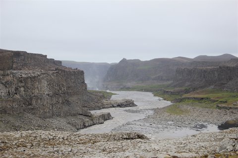 Fiume glaciale grigio scorre tra pareti rocciose sotto cielo coperto