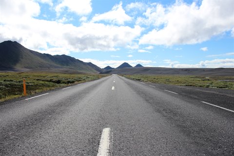 Strada deserta verso le montagne sotto nuvole bianche, Islanda