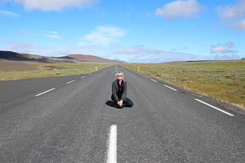 Donna in ginocchio su una strada asfaltata vuota tra la tundra
