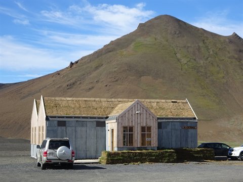 Casetta in legno con tetto di erba, montagna brulla, auto parcheggiate