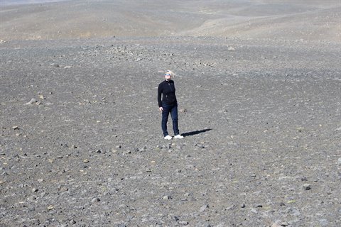 Donna sola in piedi tra pietre vulcaniche grigie sotto luce diffusa
