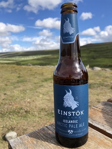 Bottiglia di birra Einstök Arctic Pale Ale su tavolo di legno, colline verdi