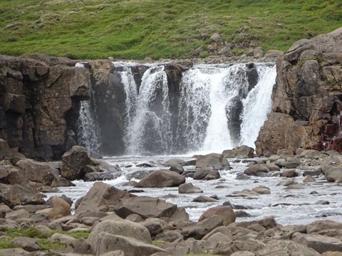 Cascata tra rocce laviche e muschio verde, acqua bianca che si frantuma