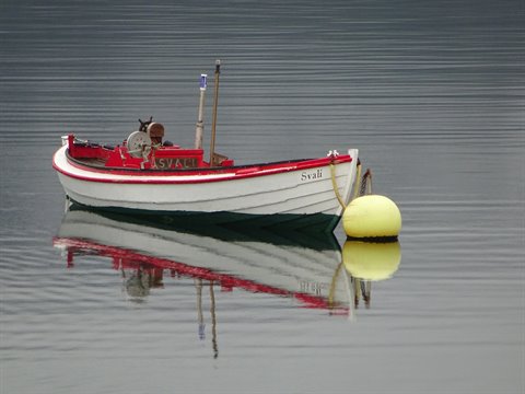 Barca da pesca rossa e bianca "Svað" ancorata a un galleggiante giallo, acqua immobile