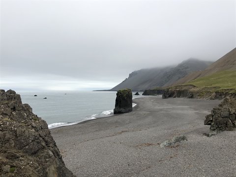 Spiaggia di sassi neri con faraglione, monti nella nebbia a Arnastapi