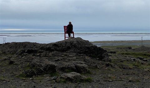 Persona seduta su sedia rossa tra rocce vulcaniche davanti alla baia