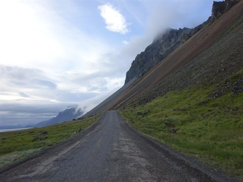 Strada sterrata sotto la montagna brulla tra nuvole basse, verso Stikkisolhmur