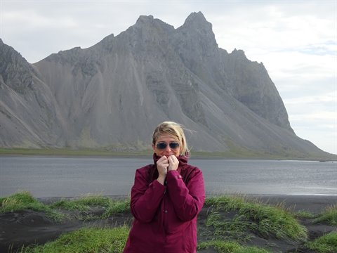 Donna con giacca granata e occhiali davanti alle vette grigie di Vestrahorn
