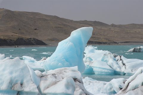 Blocchi di ghiaccio azzurro galleggiano nella laguna di Jokulsarlon, colline brune dietro