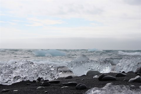Blocchi di ghiaccio trasparente sulla spiaggia nera di Jokulsarlon, onde tra le rocce