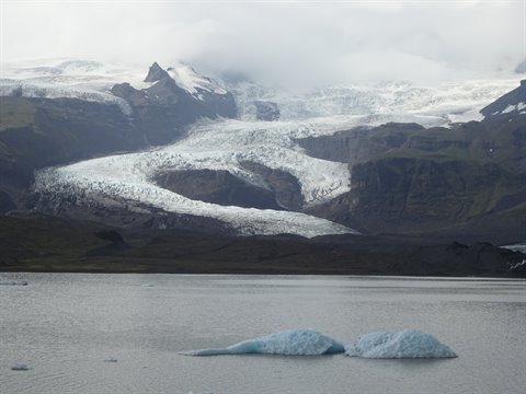 Ghiacciaio che scende tra le montagne, iceberg luminosi nel lago Fjallsarlon