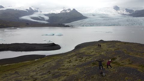 Escursione davanti al ghiacciaio Fjallsarlon, braccia alzate tra rocce e acqua
