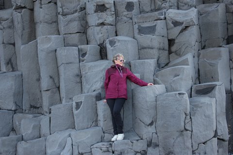 Donna in giacca bordeaux appoggiata alle colonnine di basalto a Vik