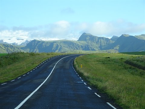Strada asfaltata che curva tra prati verdi verso montagne innevate
