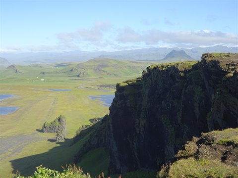 Scogliera di roccia vulcanica scura sulla verde costa di Dyrholaey