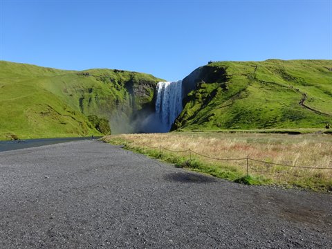 Cascata tra colline verdi vicino a Skógafoss, sentiero ghiaioso sotto il cielo azzurro