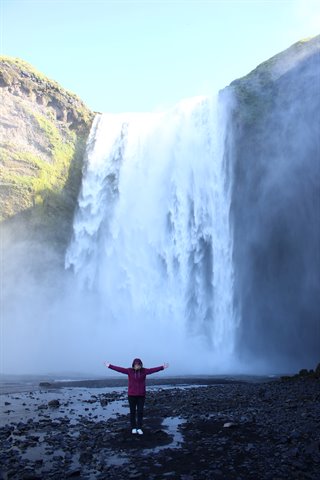 Donna con braccia aperte davanti alla cascata di Skógafoss, spruzzi e rocce nere