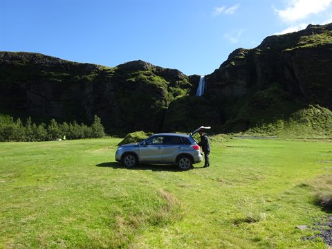 Auto parcheggiata su un prato verde con cascata sul fondo, vicino a Vik