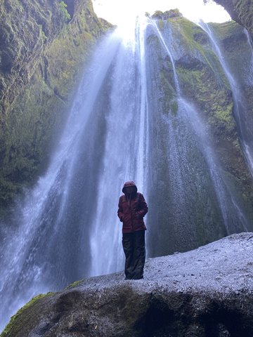 Donna con giacca rossa sotto le cascate di Gljúfrabúi