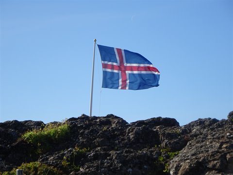 Bandiera islandesa sventola su una roccia di lava sotto cielo azzurro