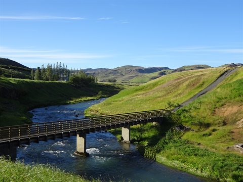 Ponte in legno e cemento sul fiume tra colline verdi, cielo azzurro