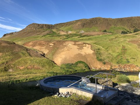 Vasca idromassaggio in pietra tra le colline verdi, luce del mattino