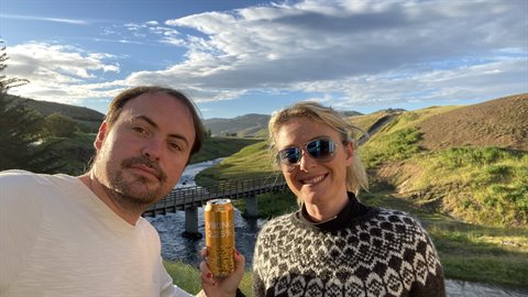 Coppia sorridente con birra e maglione islandese davanti a un ponte